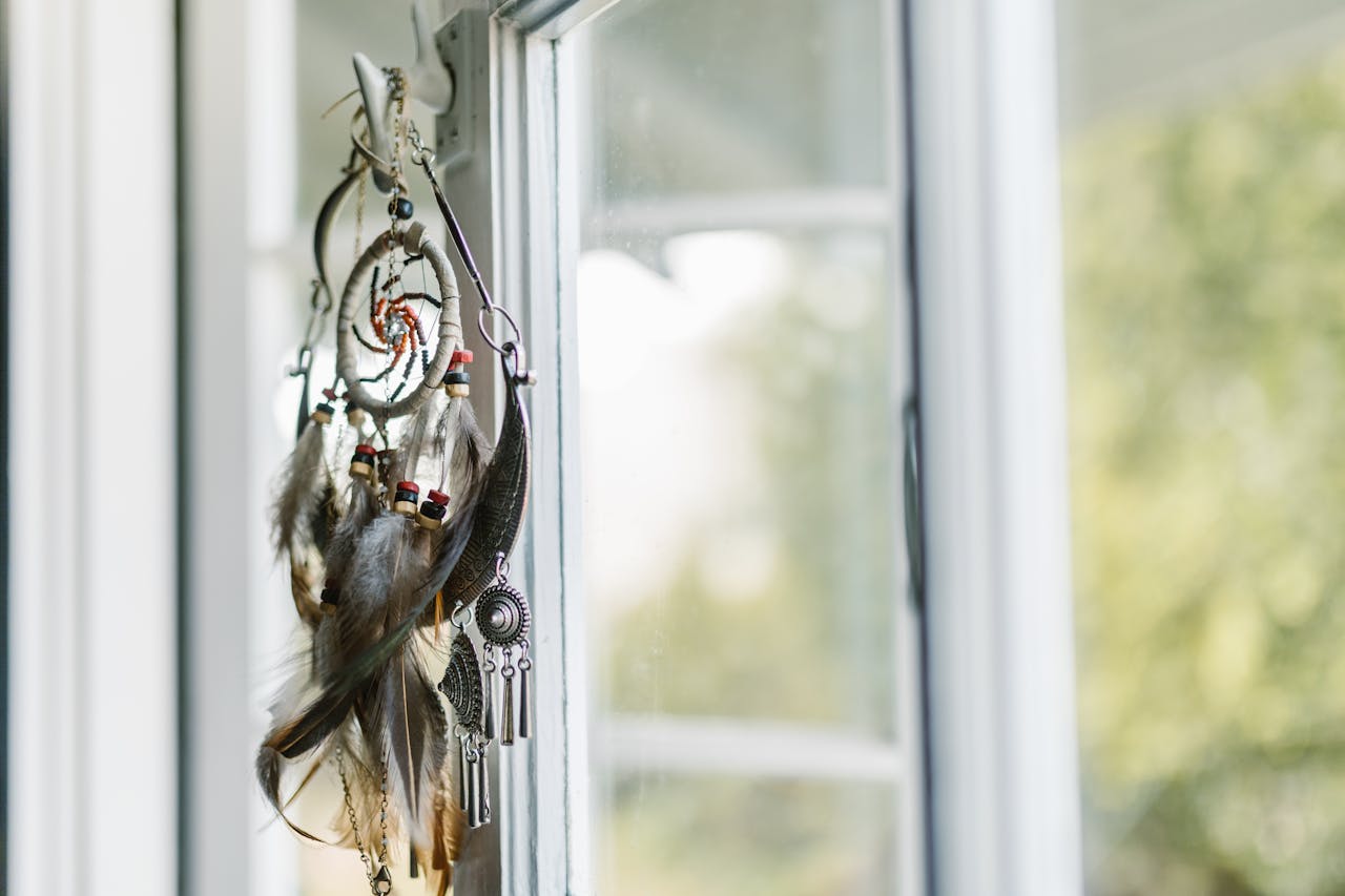 A dreamcatcher with feathers hangs by a sunlit window, creating a serene ambiance.