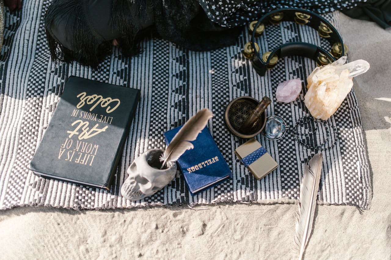 Flat lay of spiritual tools with crystals, skull cup, and feathers on a blanket outdoors.