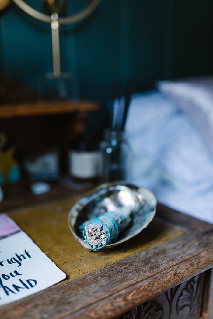 A rustic wooden table with a smudge stick in a shell, candles, and relaxing decor for a serene atmosphere.