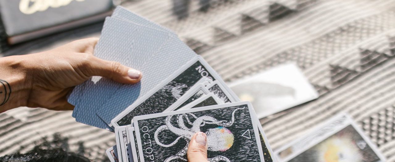 Hands holding tarot cards during a reading session on a patterned mat.